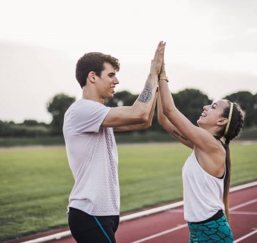 Male and female athlete high fiving on a tartan track model released Symbolfoto PUBLICATIONxINxGERxS